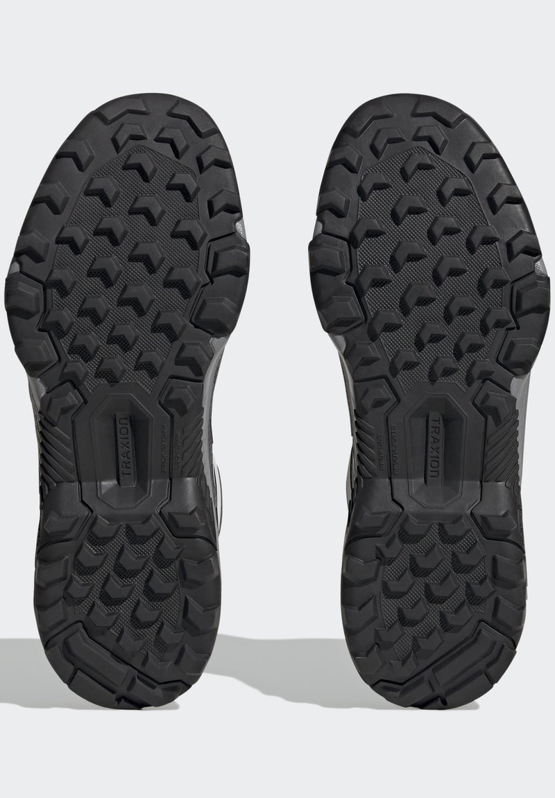 Czarne gumowe podeszwy butów z głębokim wzorem bieżnika. Zauważalne logo "TRAXION" oraz teksturowane sekcje dla lepszego uchwytu i stabilności.