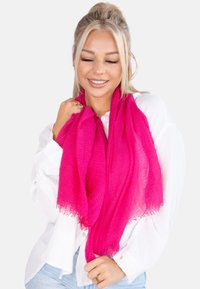 Écharpe rose vif en tissu léger et texturé, avec des bords frangés. Drapée autour du cou, elle ajoute une touche vibrante.