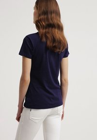 Camiseta de manga corta azul marino hecha de tejido suave. Diseño ajustado con textura suave, combinada con jeans ajustados blancos.