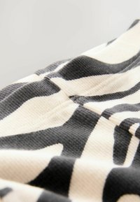 Textile à motifs zèbre en crème et noir. Surface texturée avec des rayures ondulées. Le tissu semble doux et flexible avec des détails de couture visibles.