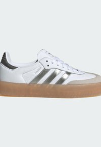Białe skórzane sneakersy z srebrnymi akcentami, teksturowaną gumową podeszwą i trzema srebrnymi paskami. Posiadają wyściełany język oraz sznurowane zapięcie.