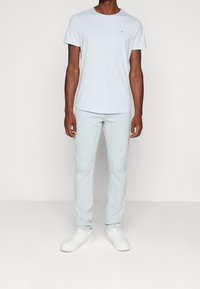 Světle modré tričko s kulatým výstřihem, spojené se světle modrými džíny a bílými teniskami. Tričko má na hrudi malé logo.