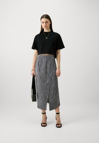 Black cropped t-shirt, gray textured wrap skirt, stacked black heeled sandals, holding a black bag. Simple, contemporary design.