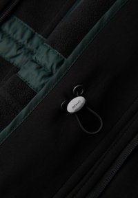 Chaqueta negra con acentos verdes, presenta una superficie texturizada, un cierre con cordón y detalles de costura en contraste.