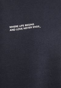 T-shirt in cotone blu scuro con texture a costine, con testo bianco: "DOVE INIZIA LA VITA E L'AMORE NON FINISCE MAI_" centrato sul petto.