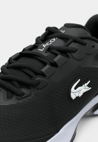 Czarny but sportowy z teksturowanym, syntetycznym wierzchem, wiązaniem na sznurowadła oraz białymi akcentami logo. Gładka podeszwa z subtelnymi wzorami.