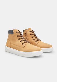 Zapatos de cuero marrón claro de caña alta con acentos en azul oscuro, suelas de goma blanca, cordones redondos y un zipper lateral para facilitar su uso.