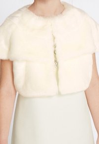 Bolero in pelliccia sintetica bianca a maniche corte indossato sopra un abito bianco senza maniche, corto al collo e alla coscia.