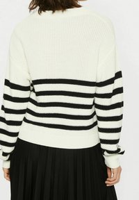 Svart och vit randig stickad tröja med ribbstruktur, avslappnad passform och sänkta axlar, i kombination med en veckad svart kjol.