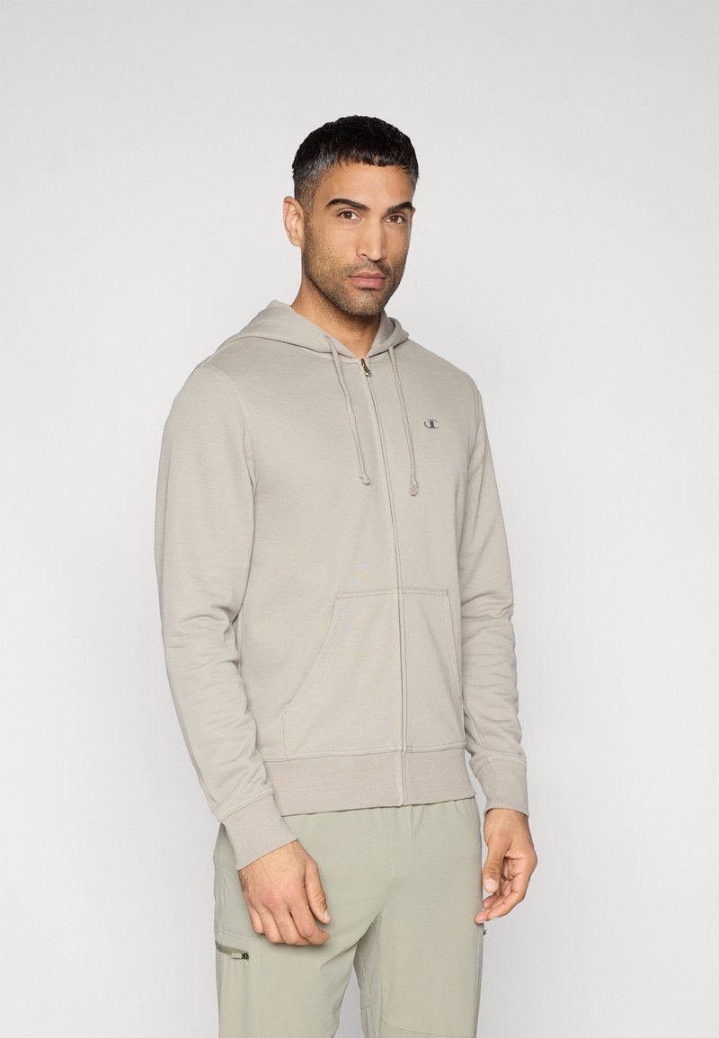 Γκρι φούτερ με φερμουάρ, εμπρόσθια τσέπη, κουκούλα με κορδόνι και μικρό λογότυπο στο στήθος. Το υλικό φαίνεται λείο και άνετο.