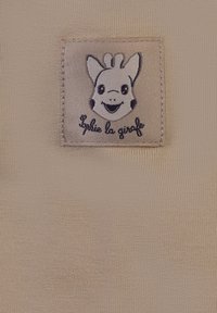 Tessuto beige con un aspetto strutturato, caratterizzato da una toppa cucita che rappresenta una giraffa sorridente e il testo "Sophie la girafe."
