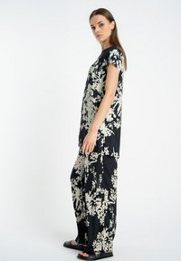 Czarny i kremowy zestaw w kwiatowy wzór, składający się z luźnej bluzki z rękawami typu cap oraz spodni z szerokimi nogawkami, wykonany z gładkiego materiału.