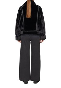 Schwarze Felljacke mit strukturiertem Design, ausgestattet mit kontrastierenden Nähten, einem breiten Kragen und kombiniert mit dunklen, weiten Jeans.