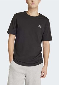 Černé bavlněné tričko s klasickým kulatým výstřihem a krátkými rukávy, s malým bílým logem adidas na levé hrudi.