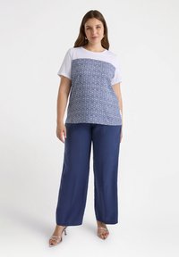 Top blanco y azul con un diseño de diamantes, combinado con pantalones acampanados de color navy. La modelo lleva sandalias plateadas con tiras.