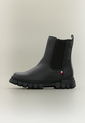 Stivaletto in pelle nera con suola spessa carrarmato, pannello laterale elastico, linguetta sul tallone e piccolo etichetta in tessuto rossa, bianca e blu.