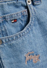 Vaaleansininen denimfarkut, joissa on etutasku, jossa on pieni punainen, valkoinen ja sininen embleemi sekä ruskealla langalla kirjailtu "Tommy".