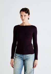 Top a maniche lunghe borgogna a coste con design a scollo barco. Vestibilità aderente, texture liscia, caratterizzato da un logo discreto sul petto. Stile casual.