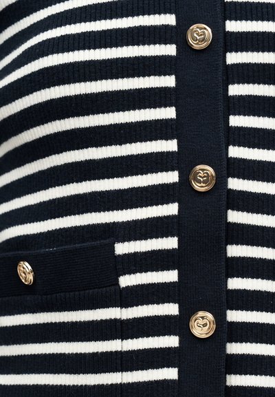 Πλεκτό ύφασμα με οριζόντιες ρίγες σε ναυτικό μπλε και λευκό, διακοσμητικά χρυσά κουμπιά και τσέπη στη αριστερή πλευρά.