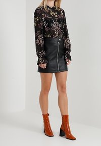 Svart blommig blus med långa ärmar, ihop med en svart läderkjol med dragkedja. Modellen bär orangea lackade ankelskor med klumpig klack.