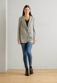 Blazer rayé de couleurs claires sur un haut noir, associé à un jean skinny bleu et des bottines noires. Tissu lisse, coupe ajustée.