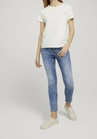 Vitt bomullströja med rund halsringning, ihopparat med ljusblå skinnyjeans och beige sneakers, som visar en avslappnad outfit.