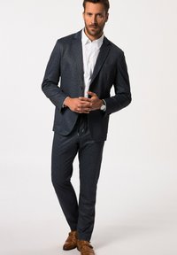 Abito blu navy con texture e vestibilità su misura, abbinato a una camicia bianca e scarpe in pelle marrone. Presenta una chiusura a un bottone e pantaloni slim.