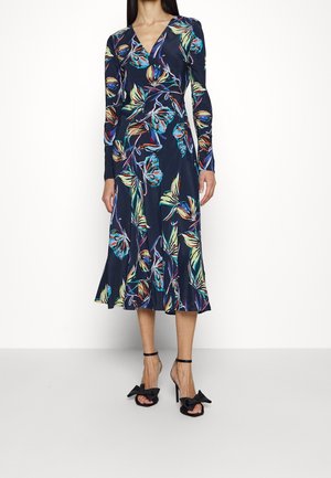 Navy blue midi dress with colorful floral print, long sleeves, V-neck, and flared hem, paired with black high-heel sandals with bow details.