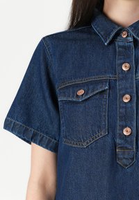 Denim overhemd in donkerblauw met korte mouwen, voorzien van twee borstzakken, gouden knopen en contrasterende stikdetails.