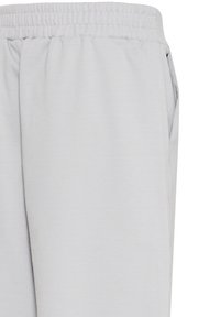 Gros plan sur un pantalon à taille élastique gris clair avec poche latérale et texture de tissu lisse.