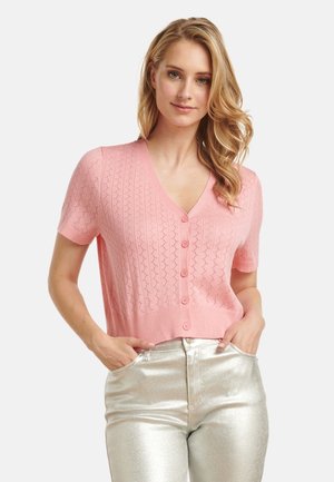 Roze gebreide cardigan met korte mouwen en een V-hals, voorzien van een knoopsluiting en een gestructureerd patroon; gecombineerd met glanzende zilveren broeken.