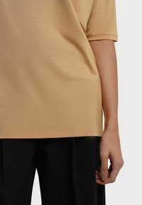 Kortærmet, lys beige top med en glat tekstur, rund kant og en afslappet pasform. Stylet med mørke, vide bukser.
