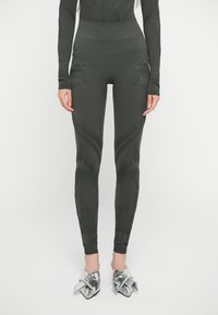 Leggings verde scuro con texture a motivo e vita alta; presenta accenti di cucitura unici lungo le gambe. Abbinati a scarpe con tacco metalliche.