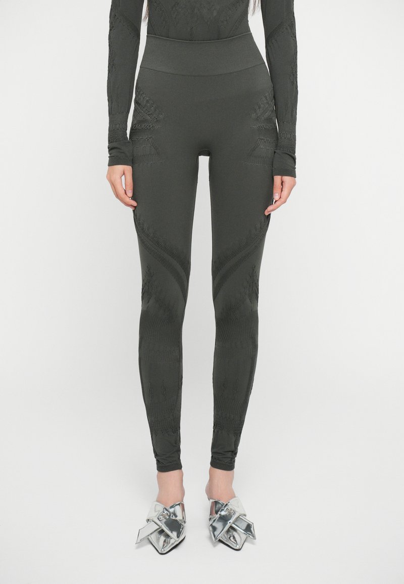 Leggings verde scuro con texture a motivo e vita alta; presenta accenti di cucitura unici lungo le gambe. Abbinati a scarpe con tacco metalliche.