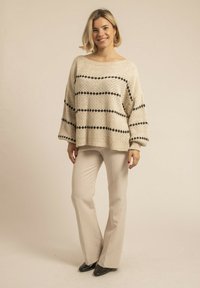 Pull en tricot beige clair avec des rayures horizontales noires, encolure large et manches longues, associé à un pantalon droit couleur crème.