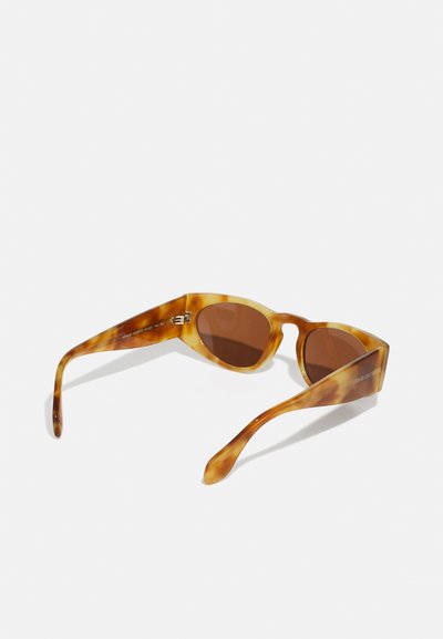 Tortoise apvalki ar kaķa acs formu, brūniem stikliem un elegantiem, sašaurinātiem kātu galiem. Iekšējā kāta daļā ir redzams logo.