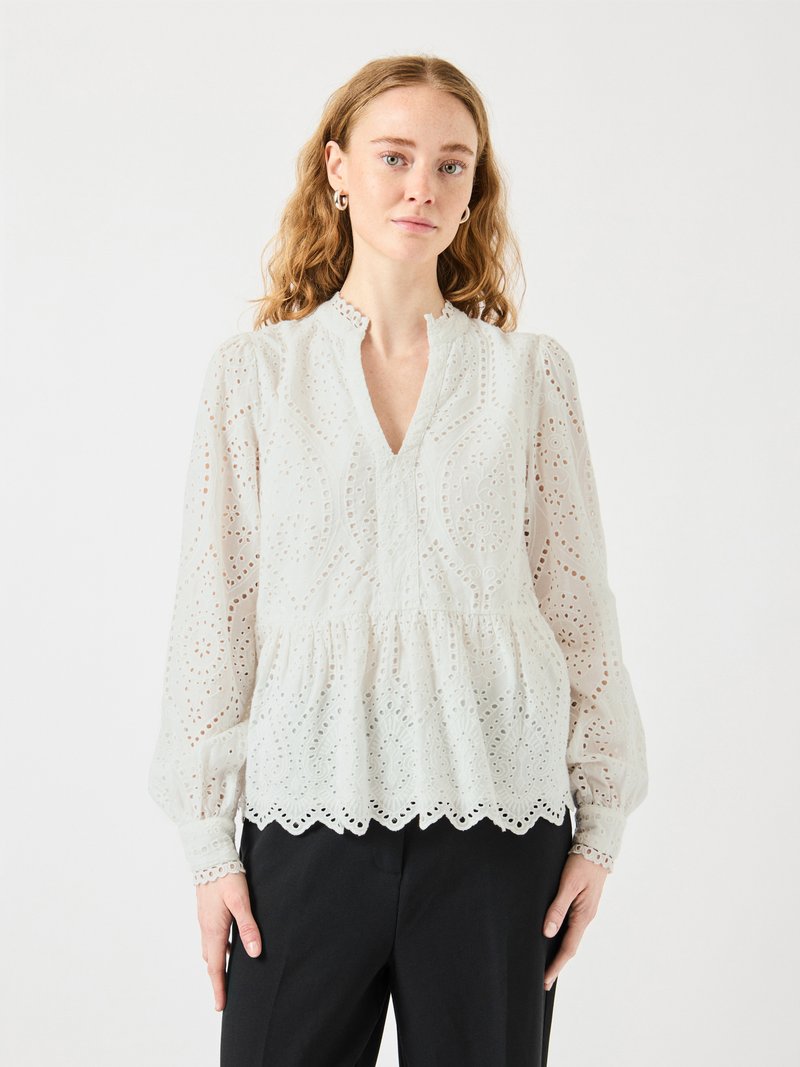 Blusa bianca in pizzo con scollo a V, vita arricciata e maniche lunghe. Presenta motivi intagliati intricati e orlo scallop.