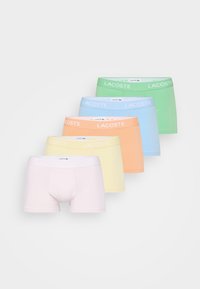 Vijf paar heren boxershorts in pastelkleuren (roze, geel, oranje, blauw, groen) met een 'Lacoste' merkband aan de taille, diagonaal gepresenteerd.