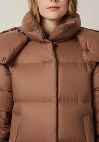 Brązowa kurtka puchowa z wysokim kołnierzem, z dużymi, wypełnionymi sekcjami, zatrzaskami i gładką, błyszczącą teksturą.