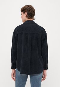 Mørkeblå langermet skjorte laget av semsket materiale med bakstykke, knappe cuffs og avslappet passform. Jeans er synlige ved kanten.