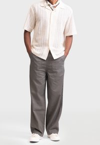 Short-sleeve, cream knit shirt with vertical stripes, paired with loose-fitting gray trousers and white sneakers.