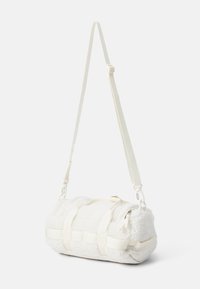 Hvit sylinderformet veske med en myk, fluffy tekstur; har justerbare stropper, minimalistisk design og en glidelås med webbingdetaljer.