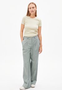 T-shirt a coste beige chiaro abbinato a pantaloni a quadri verde pallido a vita alta con chiusura a bottone e vestibilità rilassata. Scarpe bianche.
