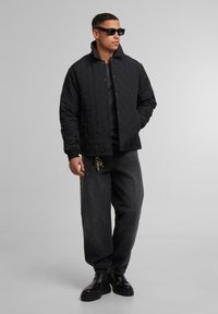 Giacca nera trapuntata con chiusura a bottoni, colletto alto e maniche lunghe. Indossata con pantaloni in denim scuri e stivaletti neri robusti.