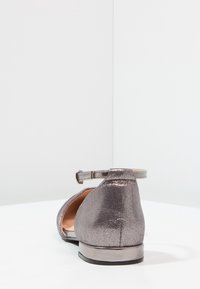 Ballerines argentées métalliques avec bride à la cheville, texture lisse, bout arrondi et petit talon. Design simple avec détails minimalistes en métal.