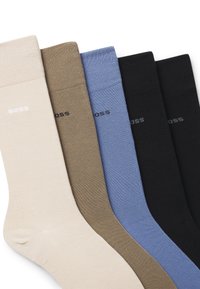 Cztery pary skarpetek załogowych w kolorach beżowym, oliwkowym, jasnoniebieskim i czarnym, o gładkiej fakturze i subtelnym czarnym logo na mankiecie.