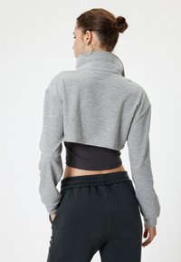 Grijze cropped sweatshirt met hoge kraag, geribbelde textuur en lange mouwen, gecombineerd met donkere broeken met elastische tailleband.
