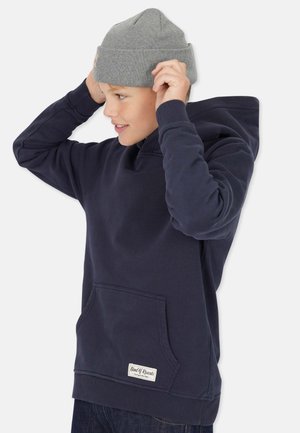 Musta fleece-huppari, jossa on etutasku, ribbaat mansetit ja harmaa neulottu pipo. Hupparissa on logopatchi lähellä taskua.