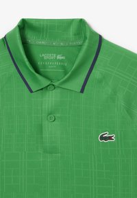 Polo verde hecho de una tela suave, con un patrón geométrico, una tapeta de tres botones y un pequeño logo en contraste en el pecho.