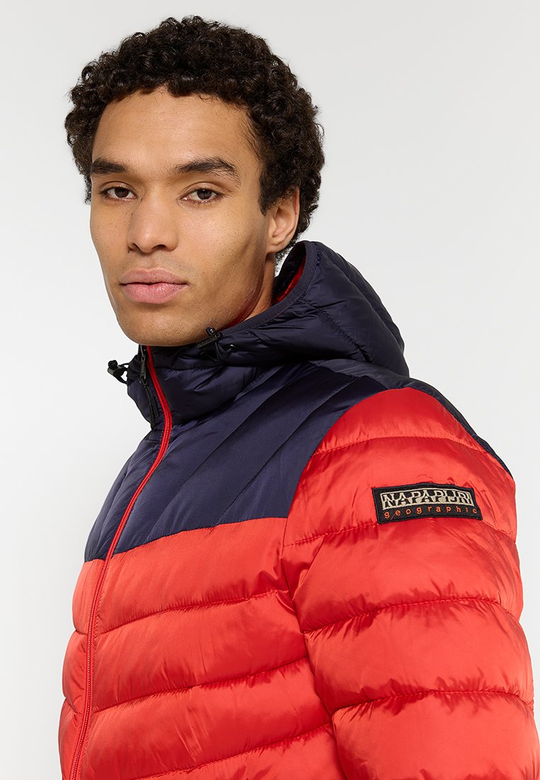 Chaqueta acolchada en rojo y azul marino con diseño de acolchado, cuello alto y capucha. Presenta un parche de logo en la manga y cierre de cremallera frontal.